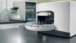 A benchtop analyser with its circular tray swung out holding small clear sample cups on a laboratory bench