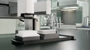 The gantry head of a benchtop liquid handling robot holding pipette tips above a tip rack and tube rack on a laboratory bench